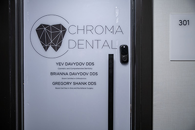 The image shows a door with signage indicating Chroma Dental, featuring a logo and names, set against an interior wall with a number 301 visible on a white panel.